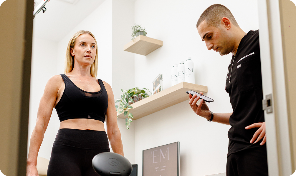 Clinician holding a handheld device beside a woman in a treatment room.