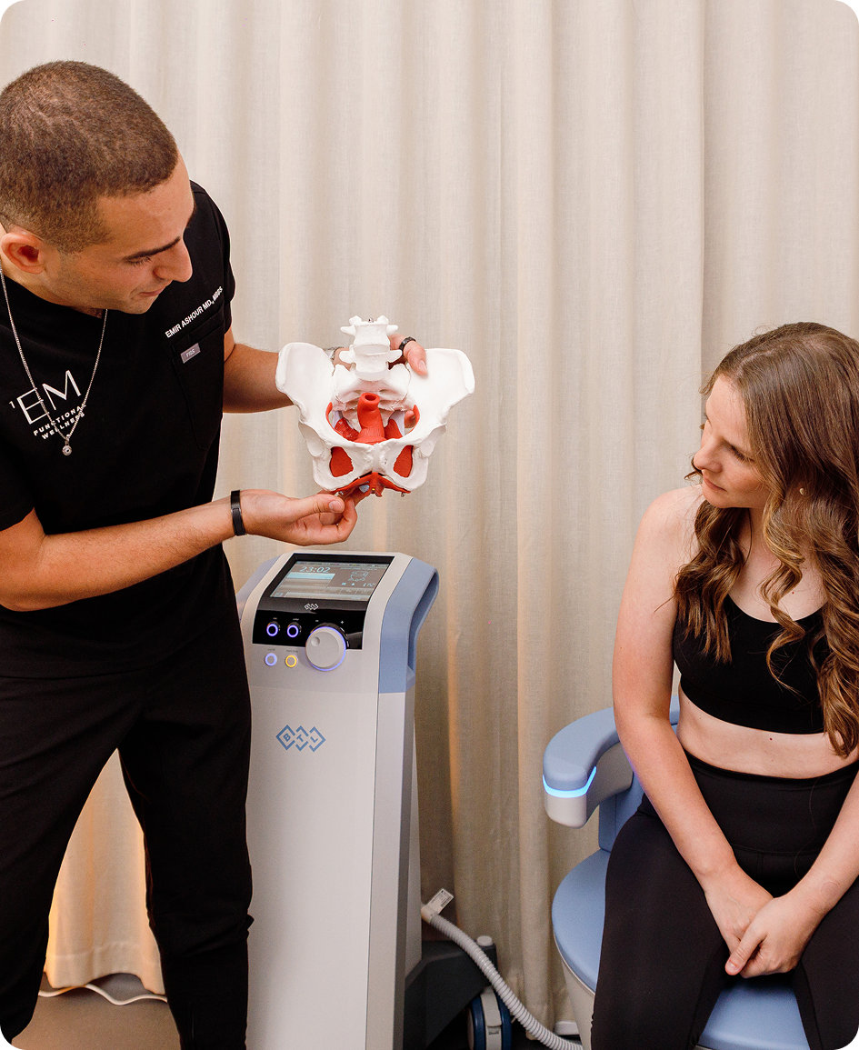 Clinician showing a pelvic anatomy model beside an EMSELLA chair.