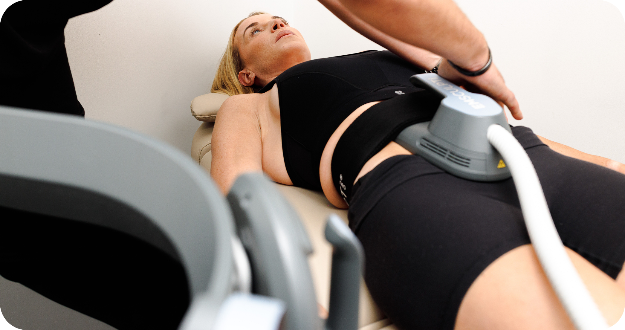 Clinician positioning an EMSCULPT NEO applicator on a woman's abdomen.