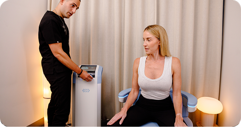 Clinician beside a woman seated on an EMSELLA chair.